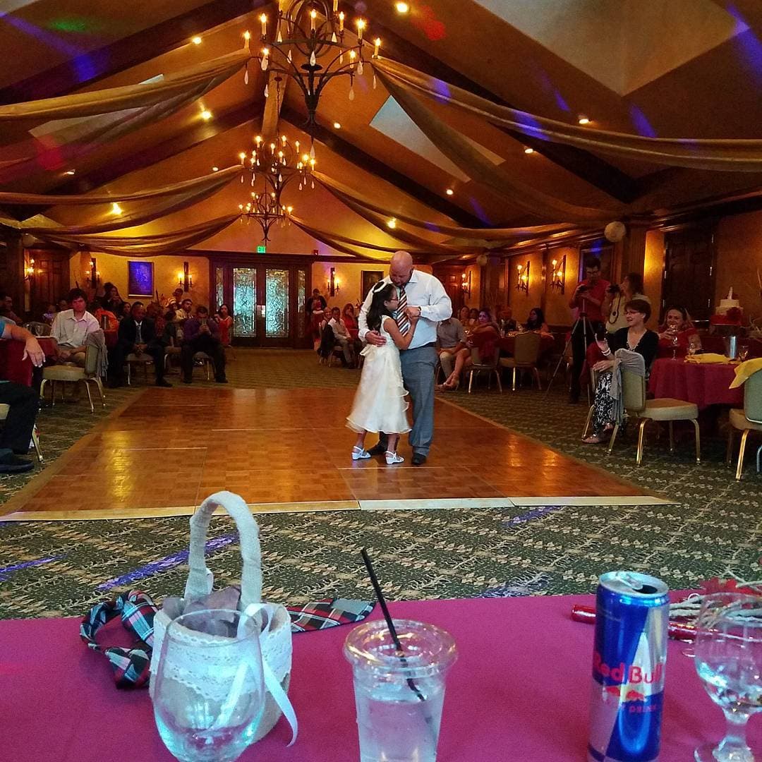 Father and young daughter share a dance on a wedding reception dance floor under chandeliers