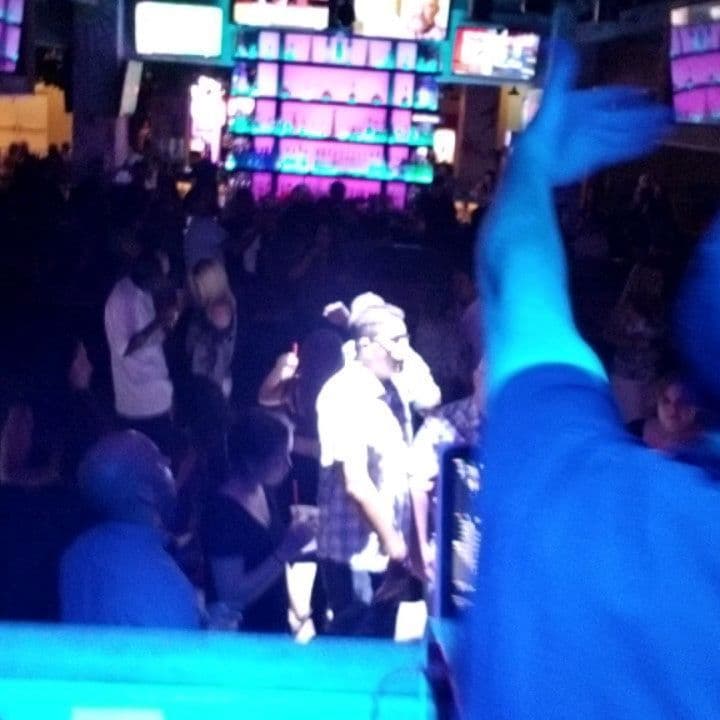 Packed nightclub dance floor under blue light with TVs and a full bar